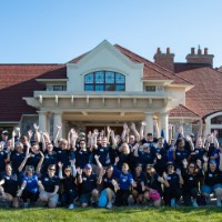 Group of excited GVSU Alumni Move in day volunteers take a group picture in front of Alumni House and Visitors Center